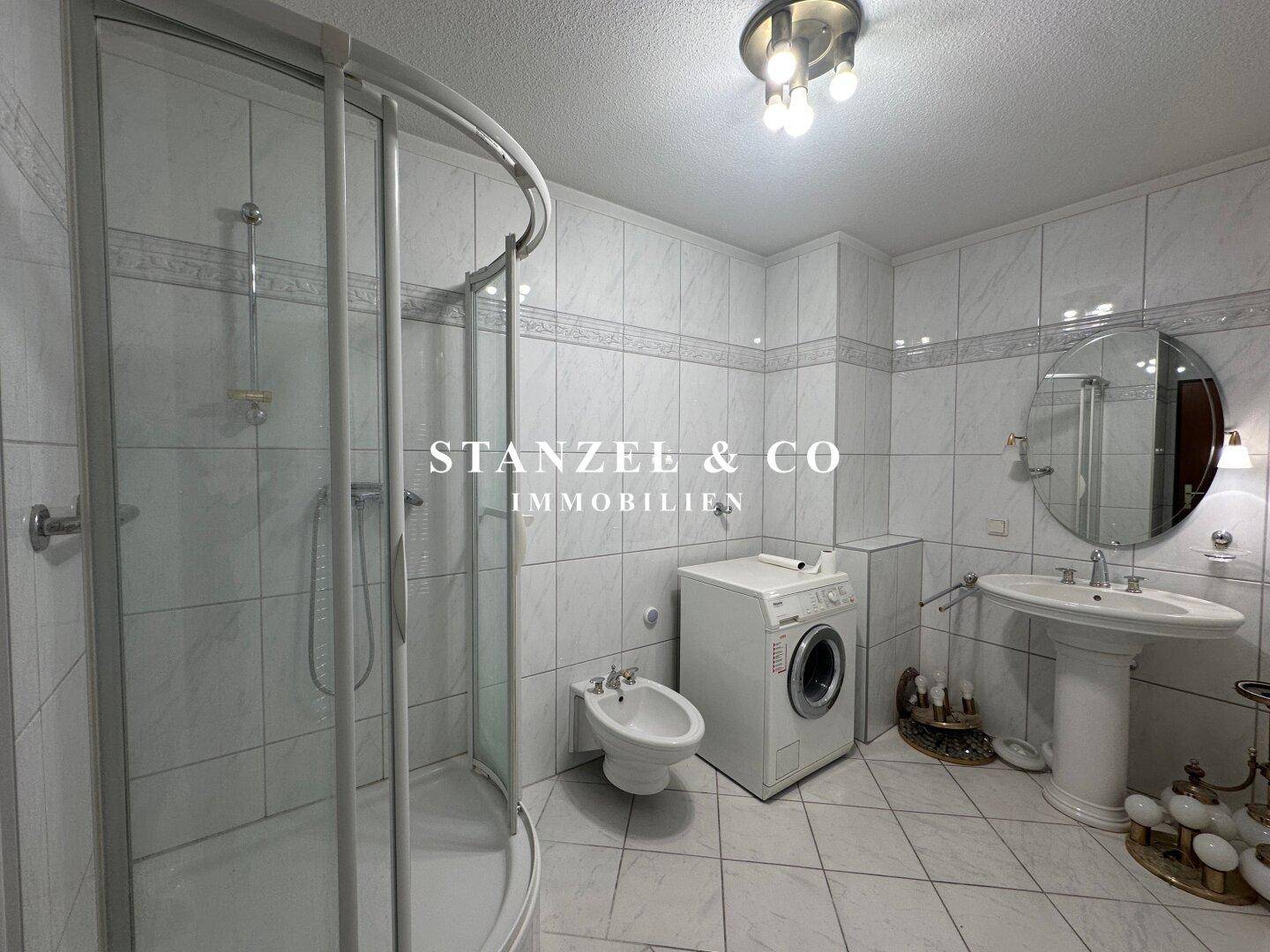 Helles Badezimmer mit Duschkabine, Bidet, Waschmaschine und großem Spiegel über dem Waschbecken.