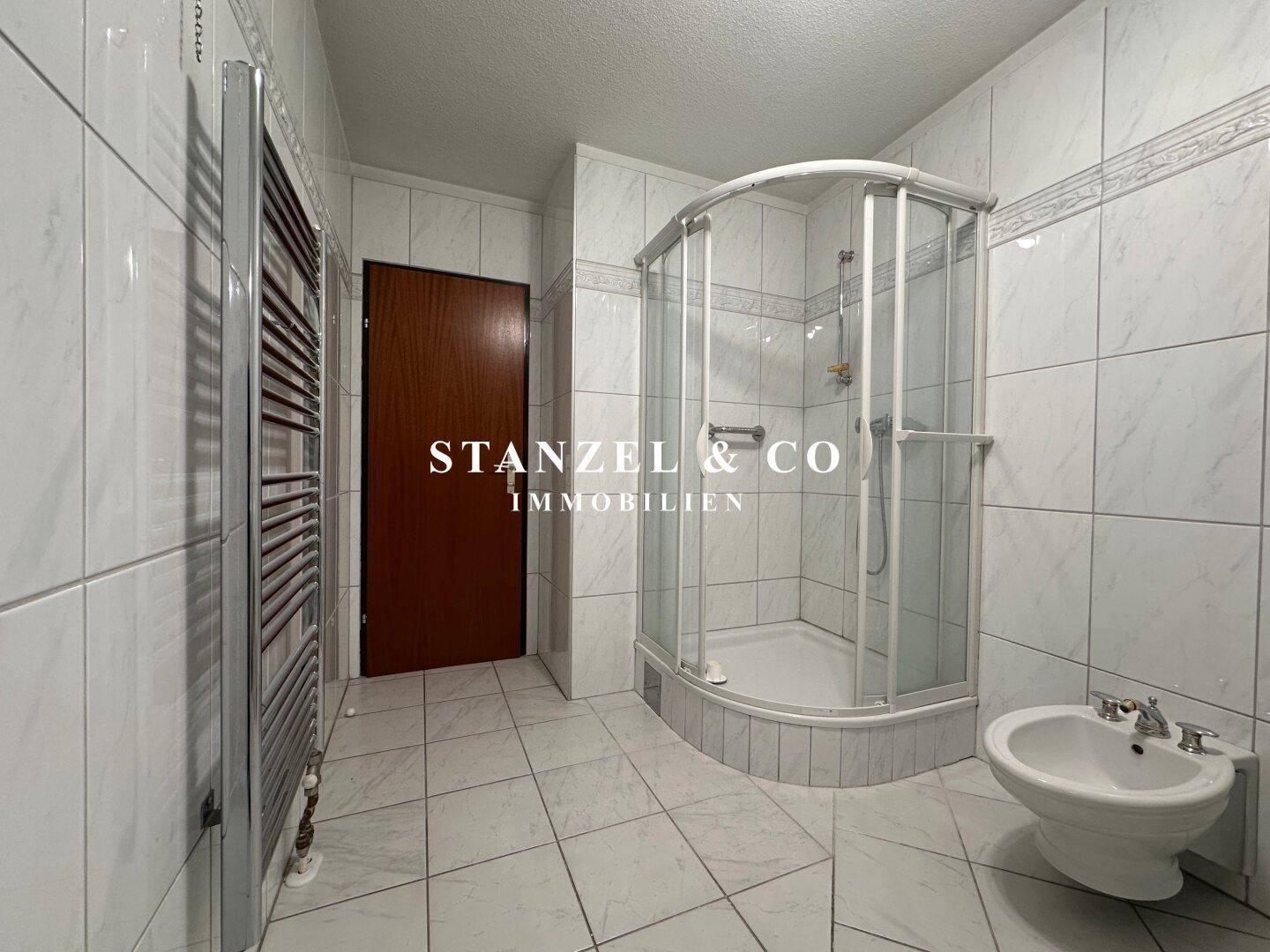 Badezimmer mit Duschkabine, Bidet und beheiztem Handtuchhalter, komplett gefliest.