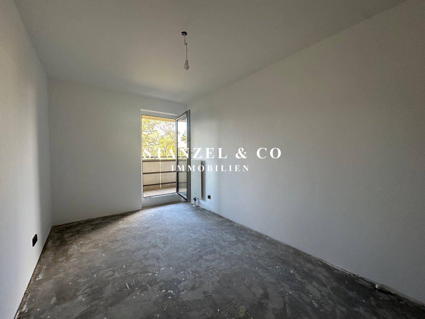 Leerer Raum mit Zugang zum Balkon, weißen Wänden und Rohfußboden, hell und offen.