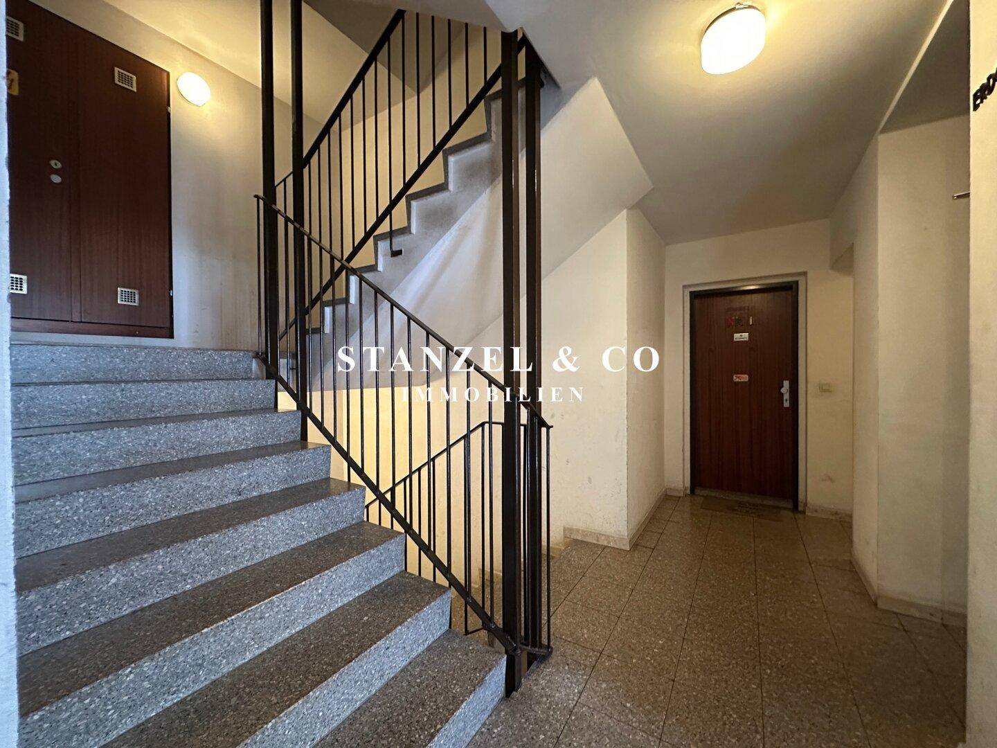 Treppenhaus mit Steinstufen und Metallgeländer in einem Mehrfamilienhaus, das zu den Wohnungen führt.