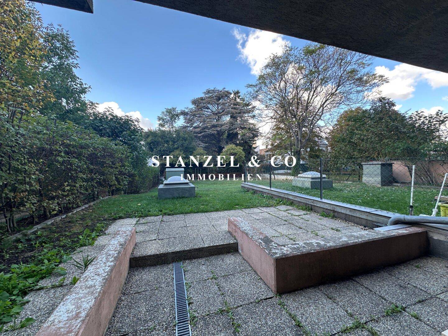 Terrasse mit Steinplatten und Blick auf den Gemeinschaftsgarten, ideal für Mahlzeiten im Freien.