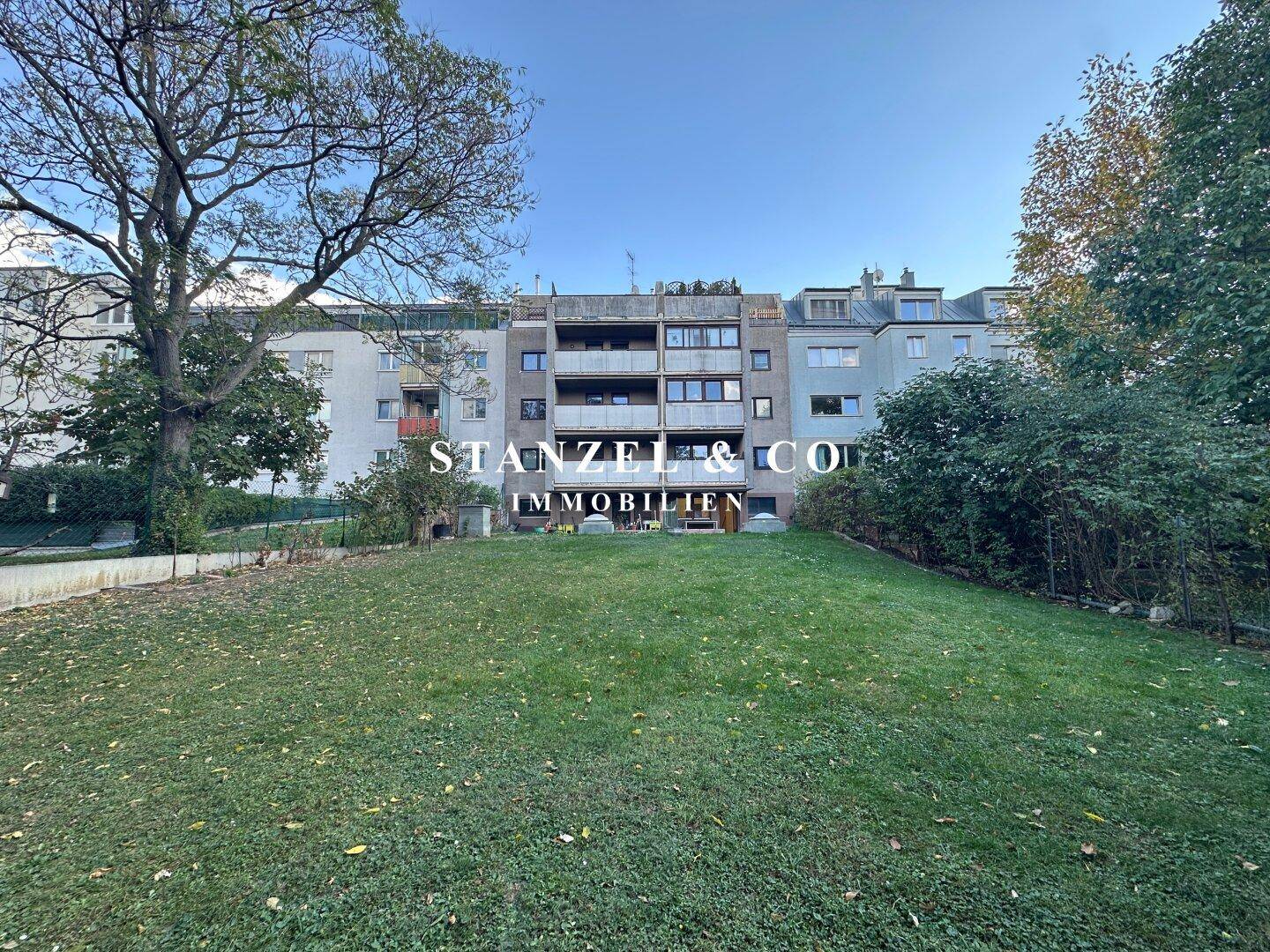 Mehrfamilienhaus mit Balkonen und großer Rasenfläche im Vordergrund, umgeben von Grün.