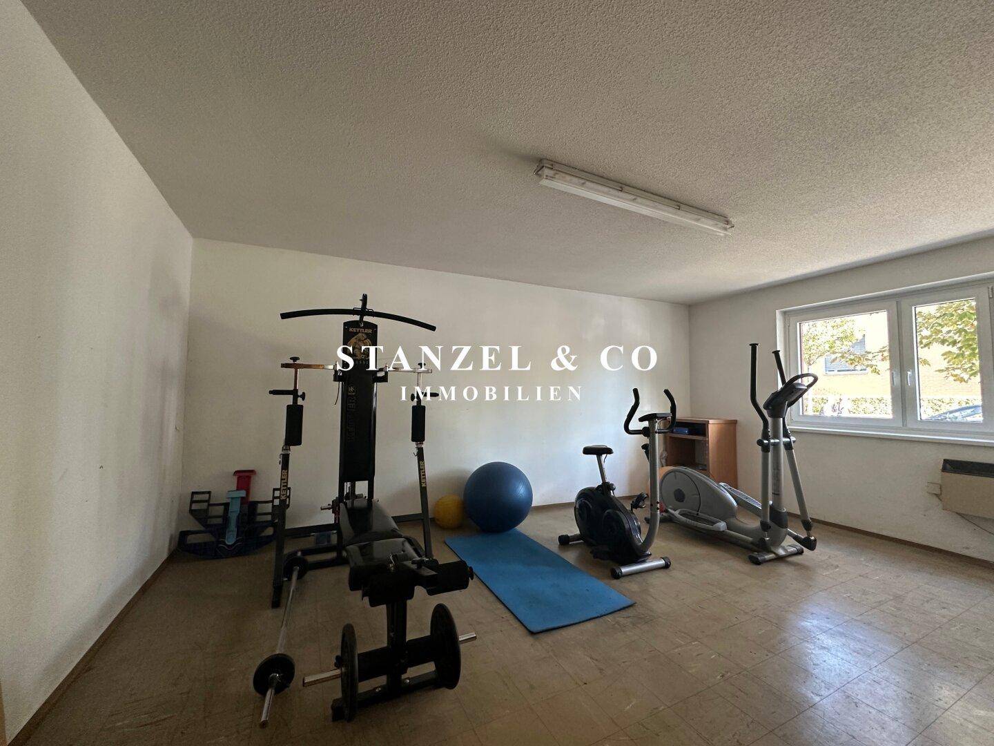 Fitnessraum mit verschiedenen Trainingsgeräten und Fenstern, ideal für sportliche Aktivitäten.