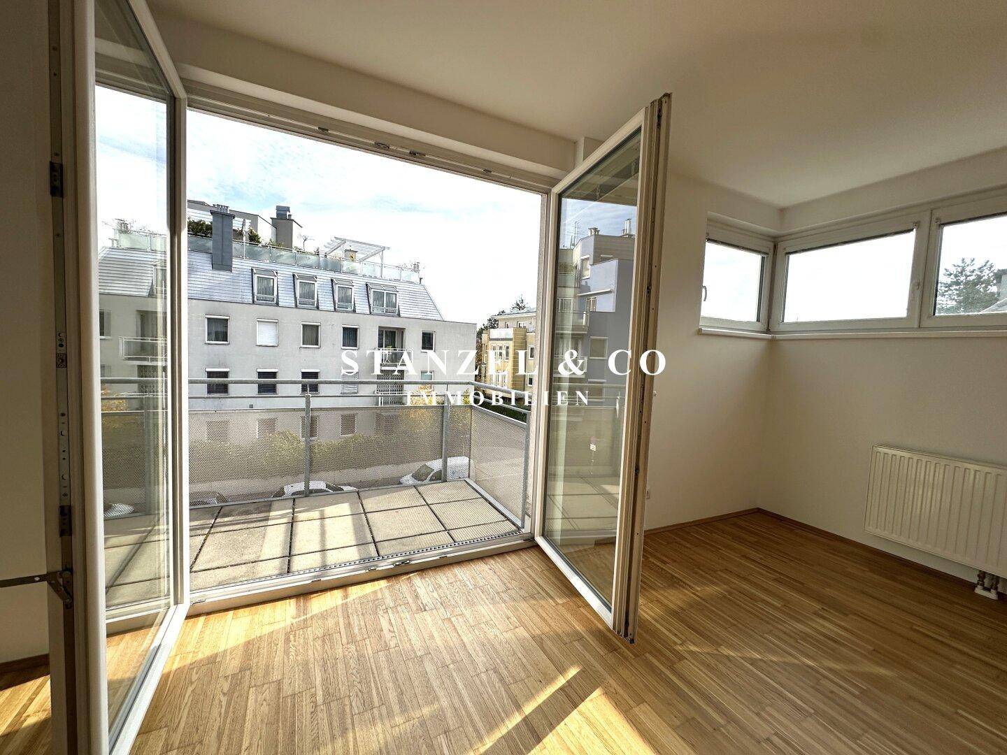 Heller Raum mit großen Fenstern und Zugang zum Balkon, bietet viel Tageslicht und Parkettboden.