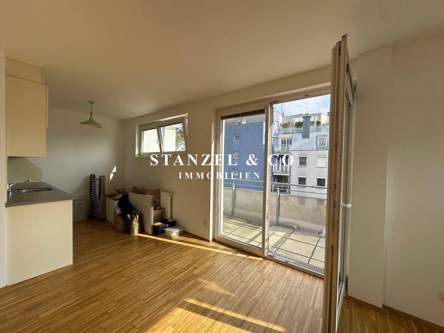 Offener Wohnbereich mit kleiner Küchenzeile und Zugang zu einem sonnigen Balkon.