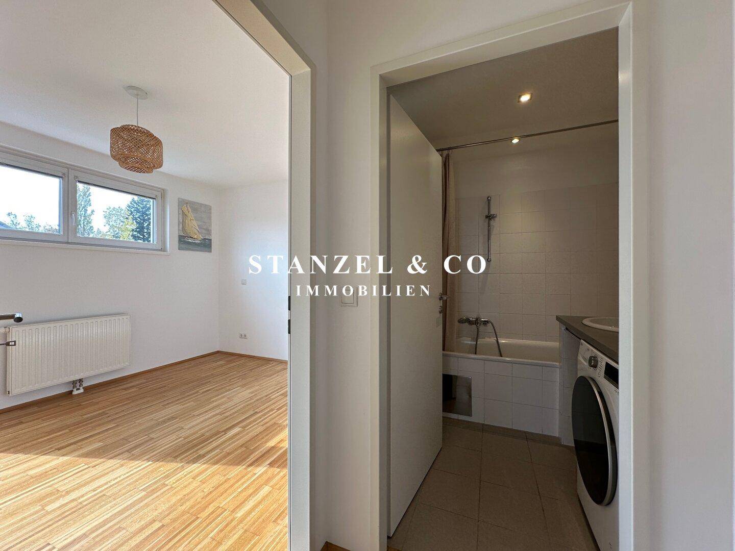 Blick vom Zimmer in ein Badezimmer mit Badewanne und Waschmaschine, hell gefliest.