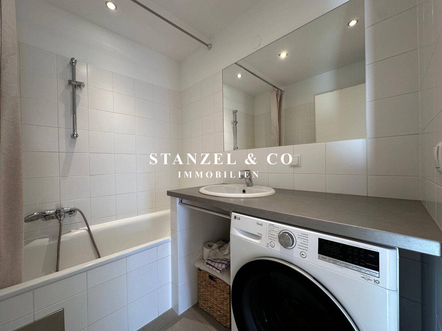 Helles Badezimmer mit Badewanne, Waschbecken und integrierter Waschmaschine, modern gefliest.