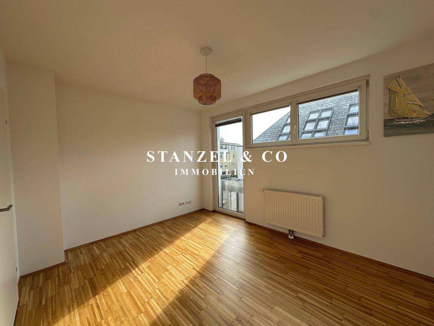 Helles Schlafzimmer mit Parkettboden und großen Fenstern, die viel Tageslicht hereinlassen.
