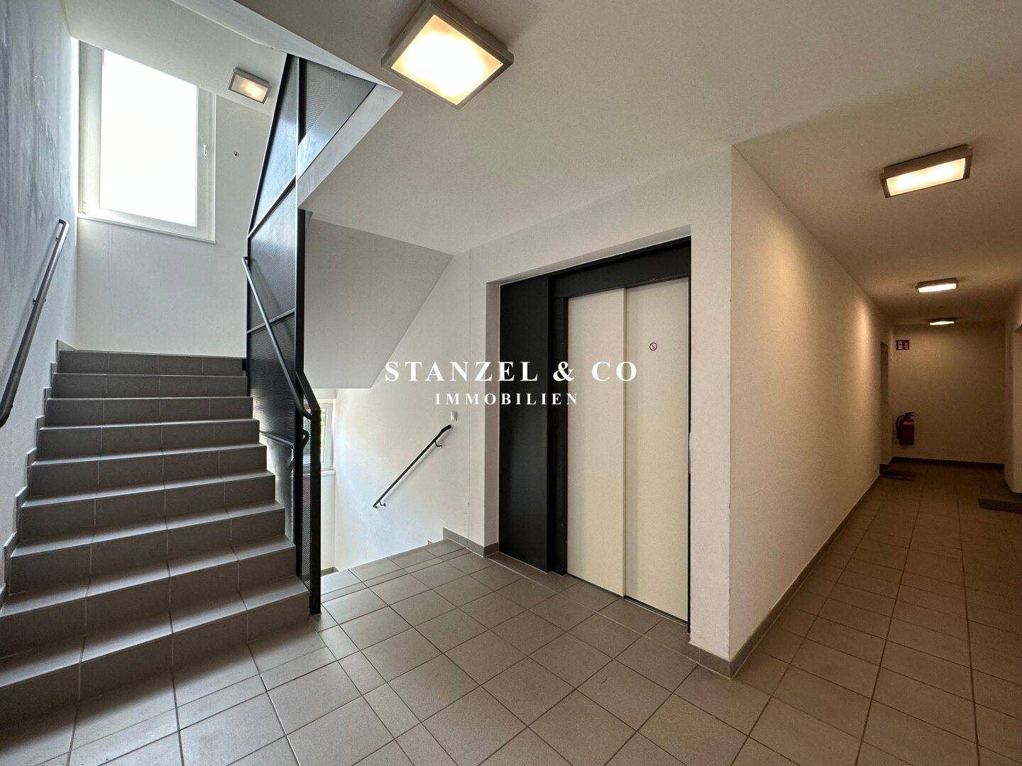 Heller Treppenhausbereich mit Aufzug und Fliesenboden in einem Mehrfamilienhaus.