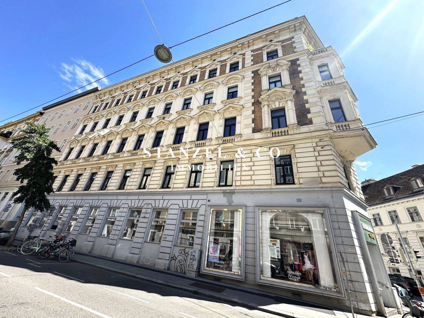 Klassisches Mehrfamilienhaus mit detaillierter Fassade und Geschäften im Erdgeschoss an einer städtischen Straße.