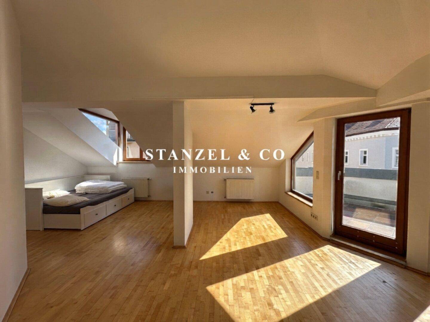 Schlafzimmer im Dachgeschoss mit Holzboden, schrägen Wänden und Zugang zur Terrasse.