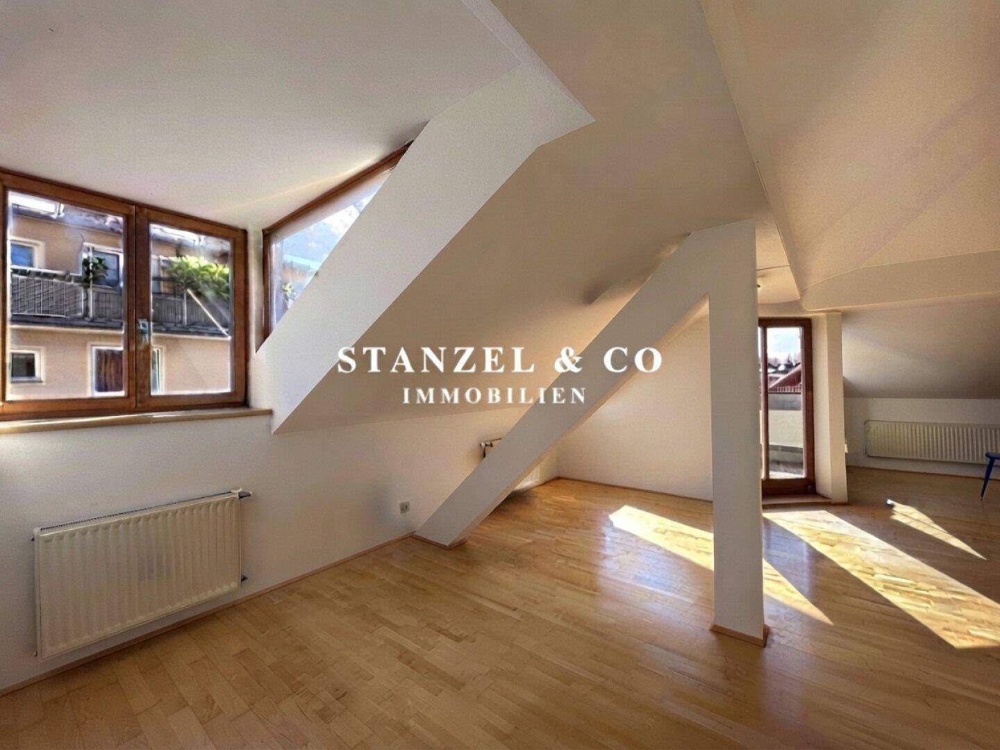 Heller Dachgeschossraum mit Holzboden, schrägen Wänden und großen Fenstern.
