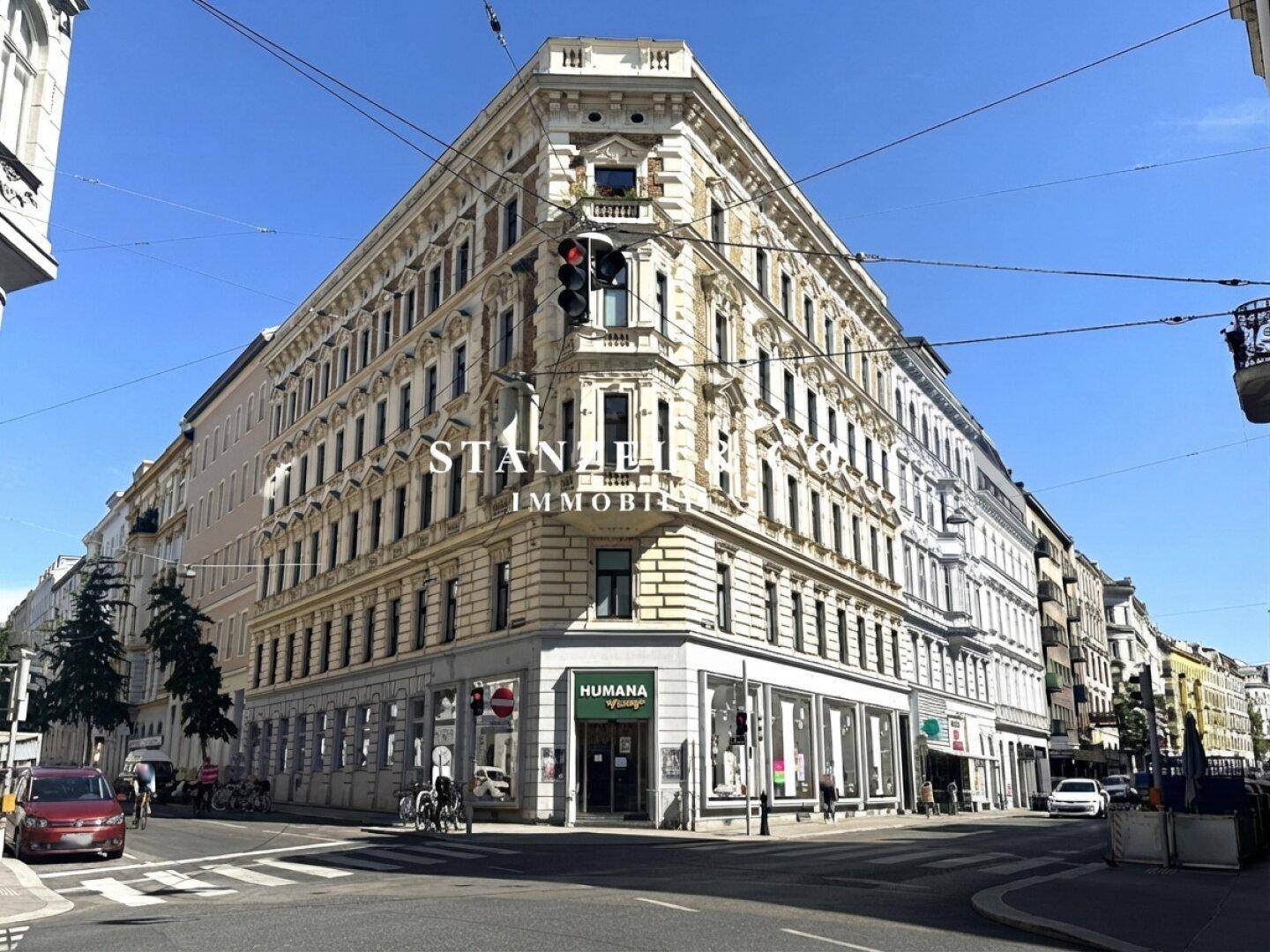 Historisches Eckgebäude mit detaillierter Fassade und Geschäften im Erdgeschoss unter blauem Himmel.