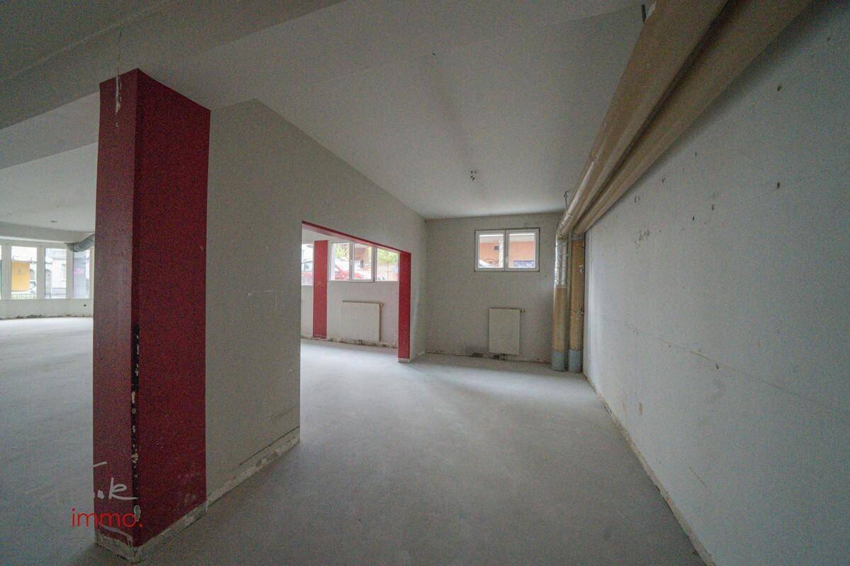 Innenansicht eines Teils des Gewerberaums mit weißen Wänden, Betonboden und einem Fenster.