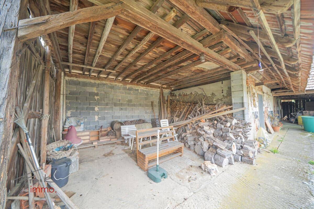 Rustikaler überdachter Bereich mit Holzbalken und Lagerplatz, in ländlicher Umgebung.