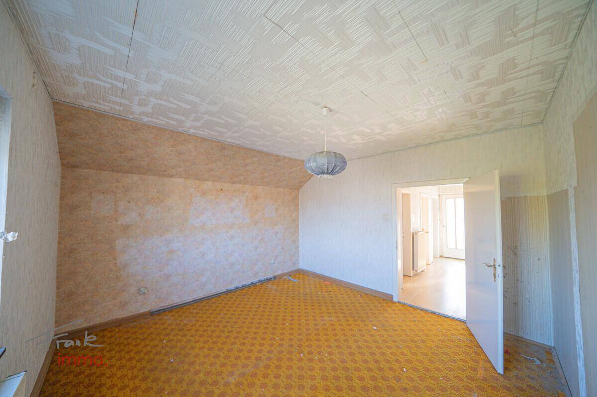 Dachzimmer mit schräger Decke, gelbem Teppichboden und renovierungsbedürftigen Wänden im Obergeschoss.
