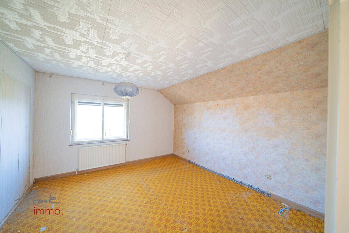 Helles Dachzimmer mit Fenster, schräger Decke und gelbem Teppichboden, ideal für ein Kinderzimmer.