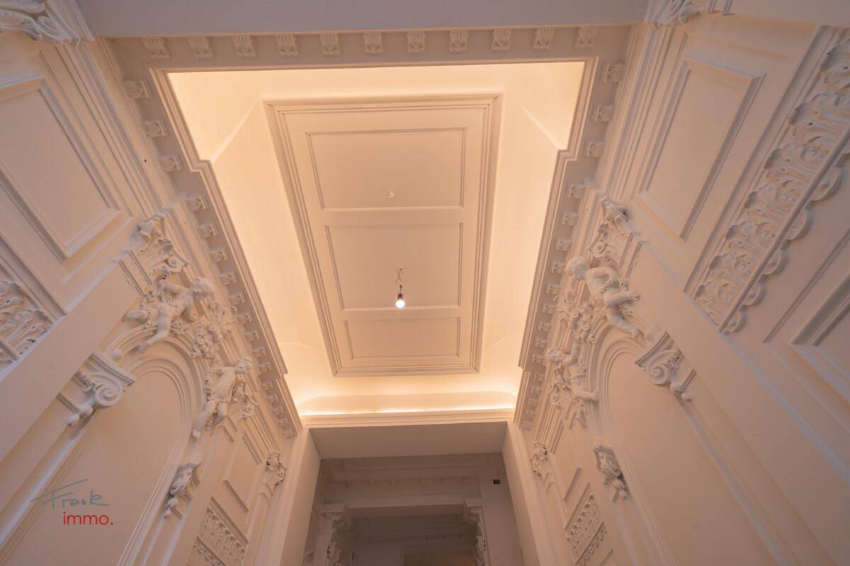 Detailaufnahme der aufwendigen Stuckdecke und indirekten Beleuchtung im historischen Flur.