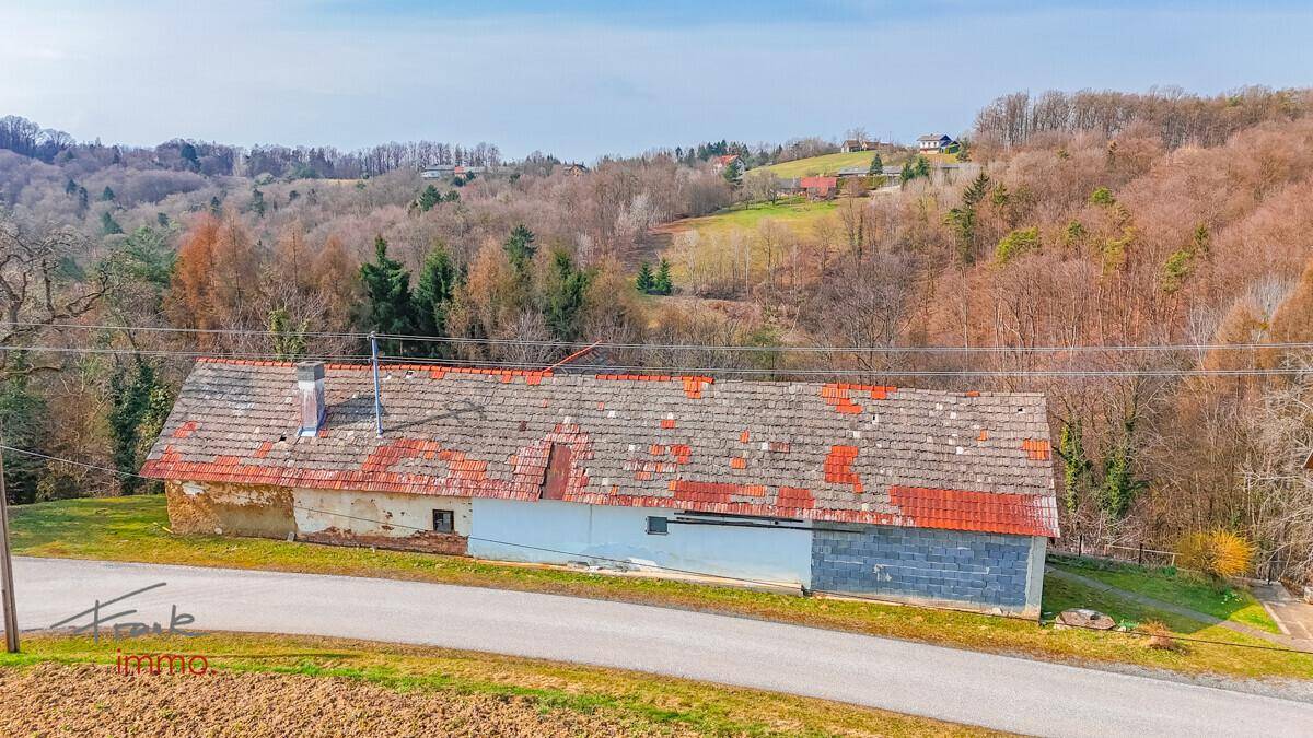 Luftaufnahme einer langen Scheune mit altem Ziegeldach, umgeben von Feldern und Wald.