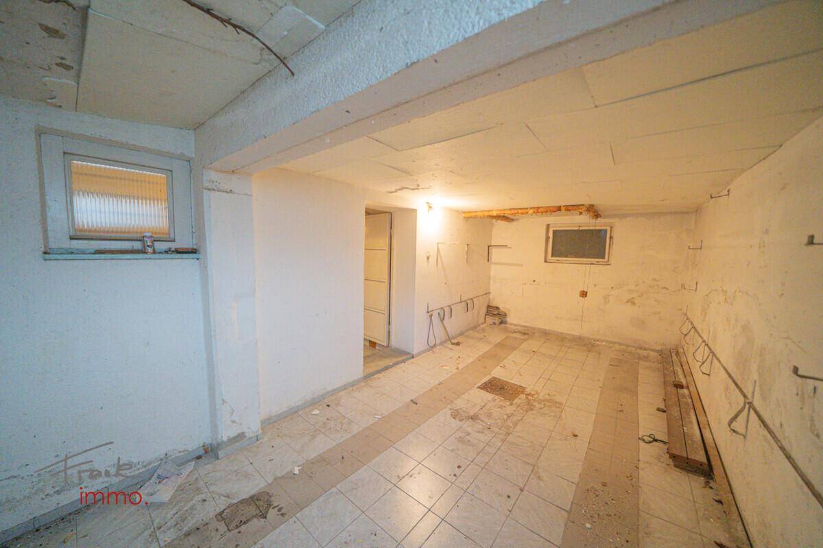 Großer Garagen- oder Abstellraum mit Fenster, Fliesenboden und sichtbaren Installationen.