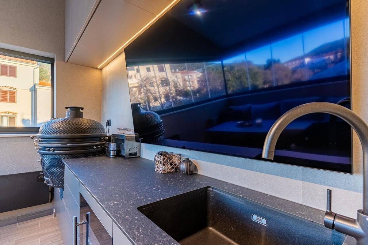 Moderne Außenküche mit Grill, Spüle und Blick auf die Umgebung.