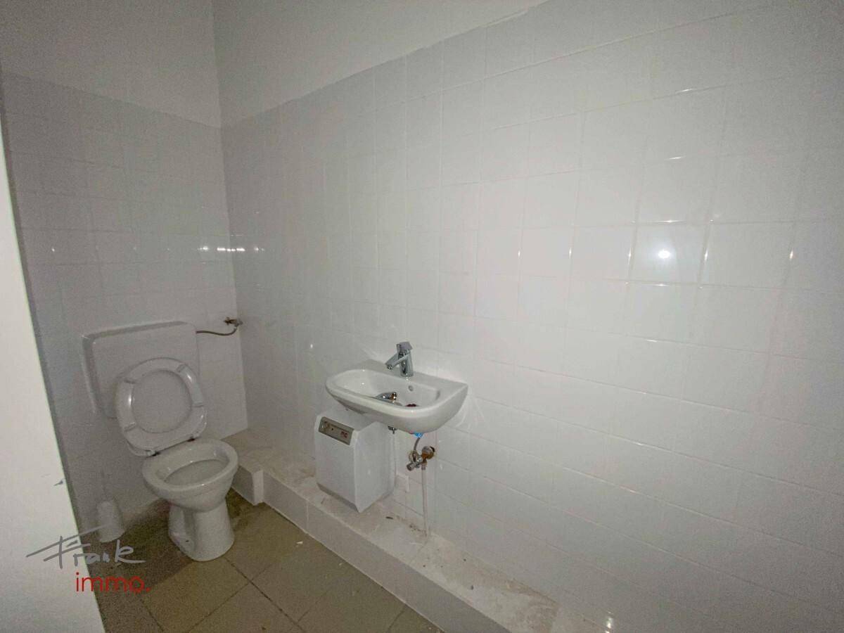 Saubere Toilette mit weißen Fliesen an den Wänden und einem kleinen Waschbecken.