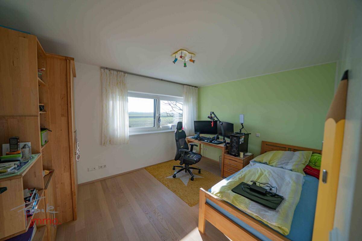 Helles Kinderzimmer mit Schreibtisch, Holzboden und Blick ins Grüne.