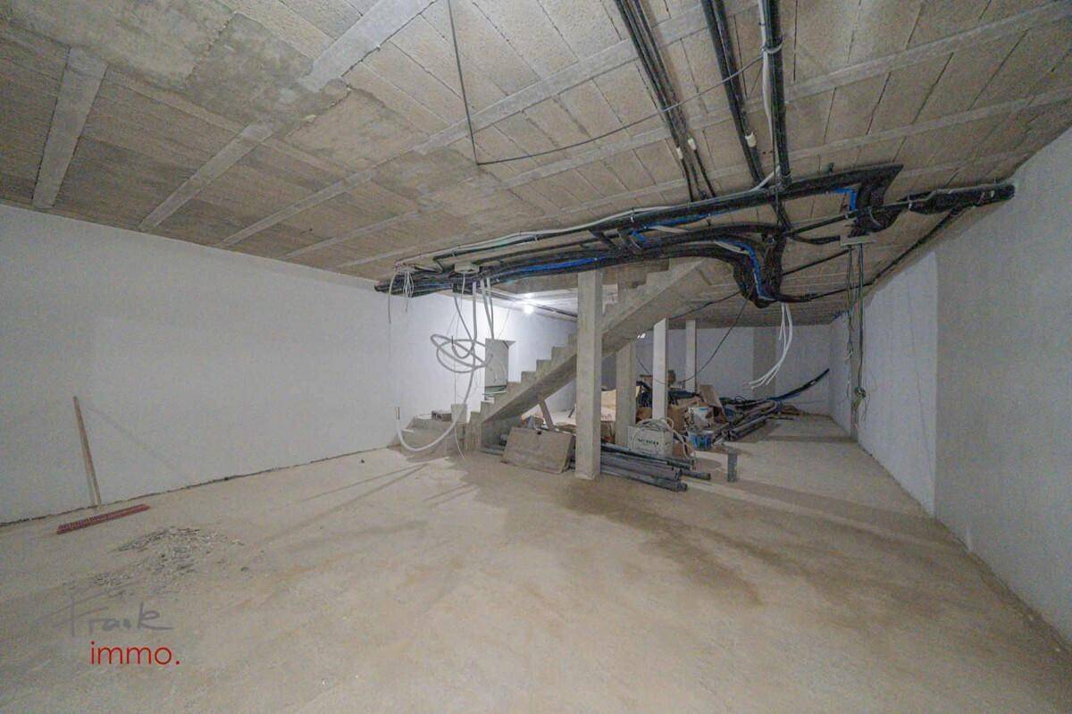 Kellerbereich im Rohbau mit sichtbaren Treppen, Rohrleitungen und Betonstrukturen.
