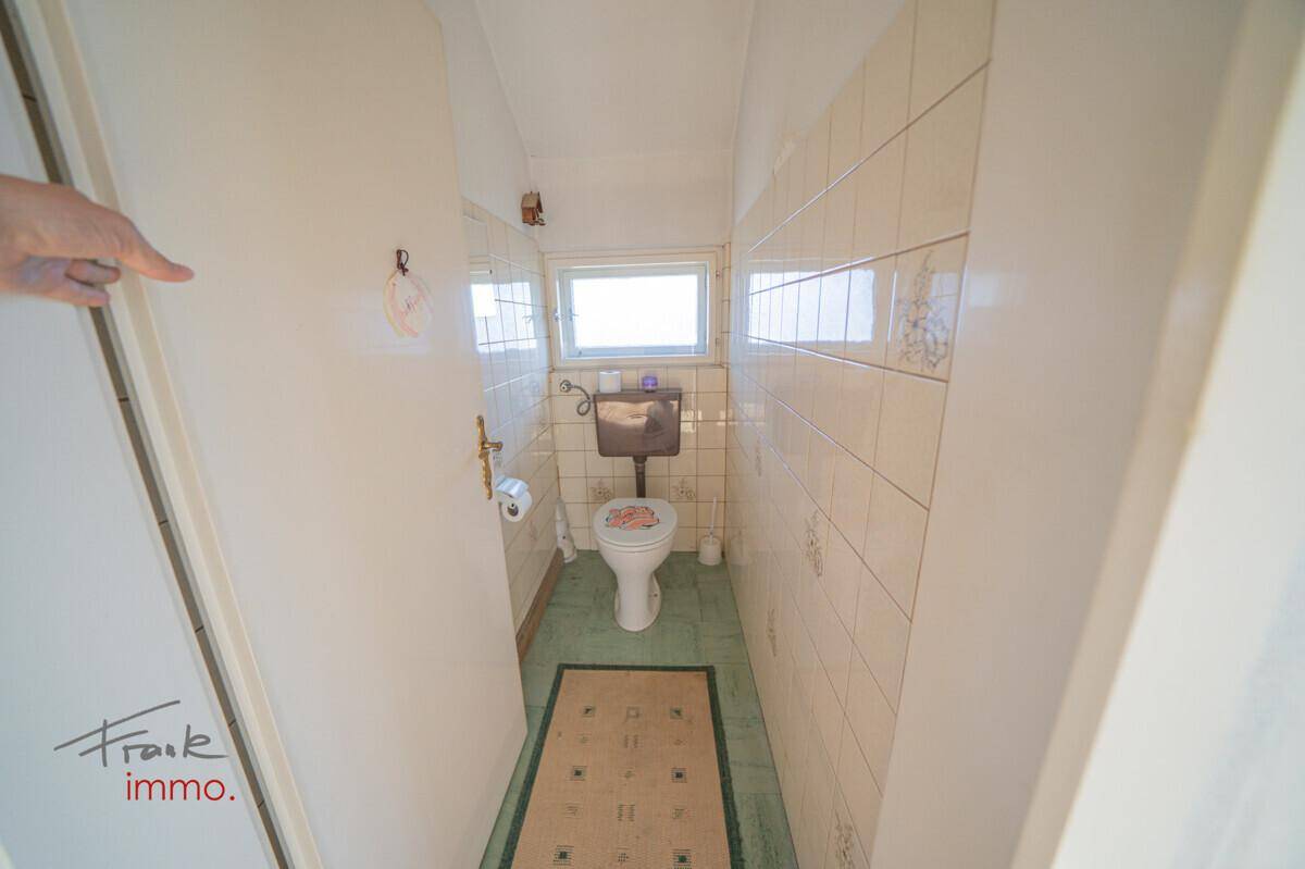Kleines Gäste-WC mit Toilette, grünen Bodenfliesen und Fenster, ideal für eine schnelle Renovierung.