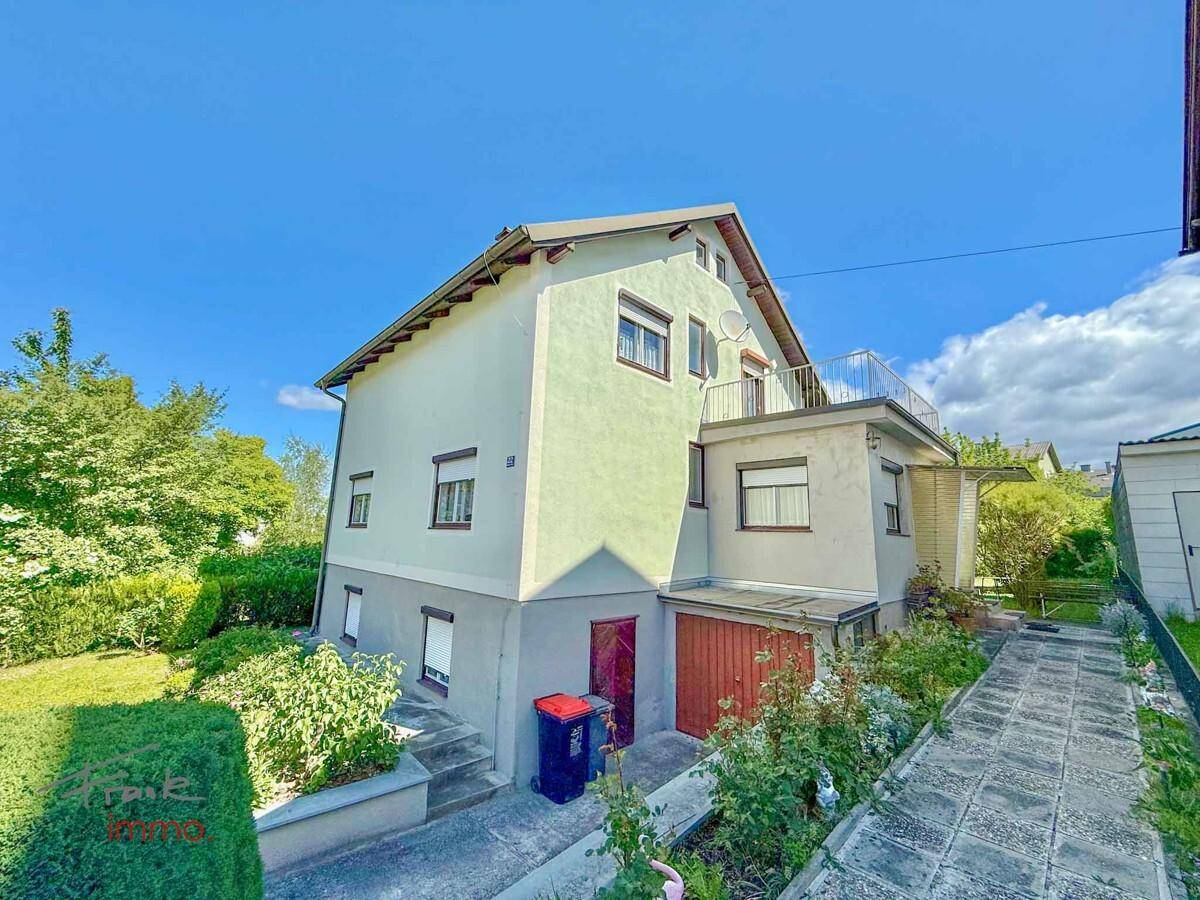 Einfamilienhaus mit Garten, Auffahrt und einem kleinen Balkon unter blauem Himmel.