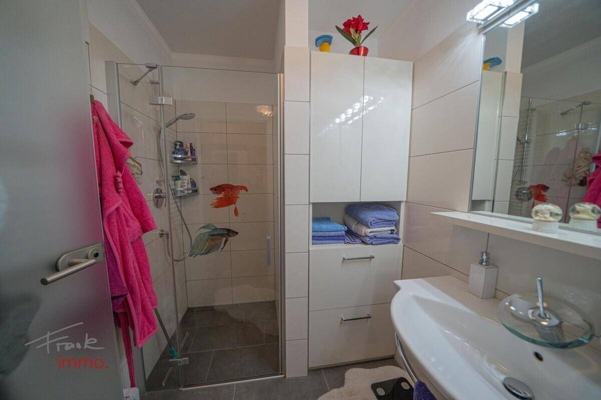 Helles Badezimmer mit Duschkabine, modernem Waschbecken und weißen Schränken.