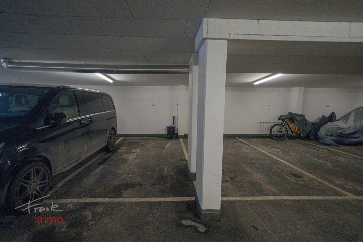 Tiefgarage mit Stellplätzen für Fahrzeuge und Fahrräder, beleuchtet durch Deckenleuchten.