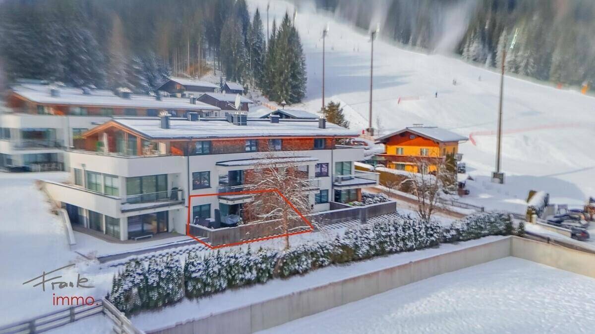 Winteransicht der modernen Wohngebäude in verschneiter alpiner Umgebung mit Skipisten im Hintergrund.