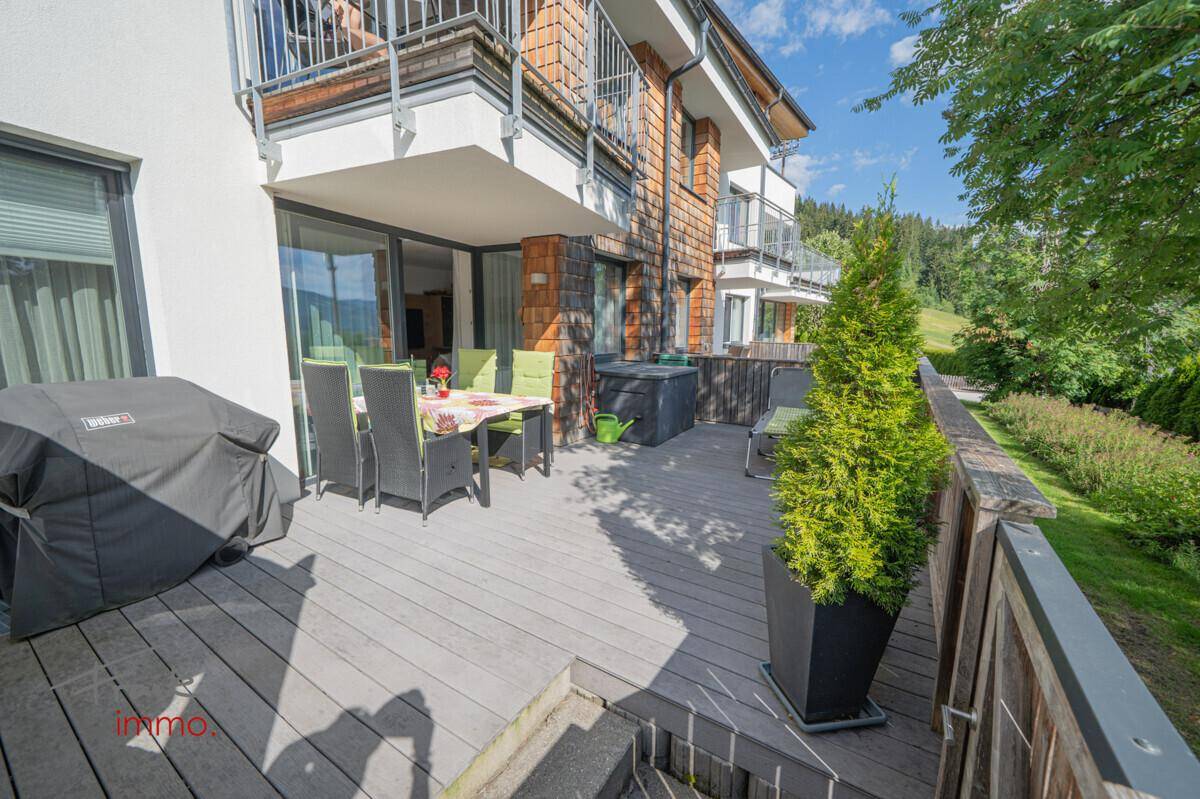 Sonniger Terrassenbereich mit Esstisch, Grill und Blick auf die grüne Berglandschaft.