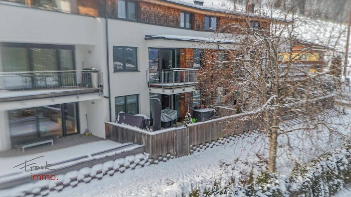 Winterliche Terrasse mit Schnee bedeckt, umgeben von Bäumen und einem Holzzaun.