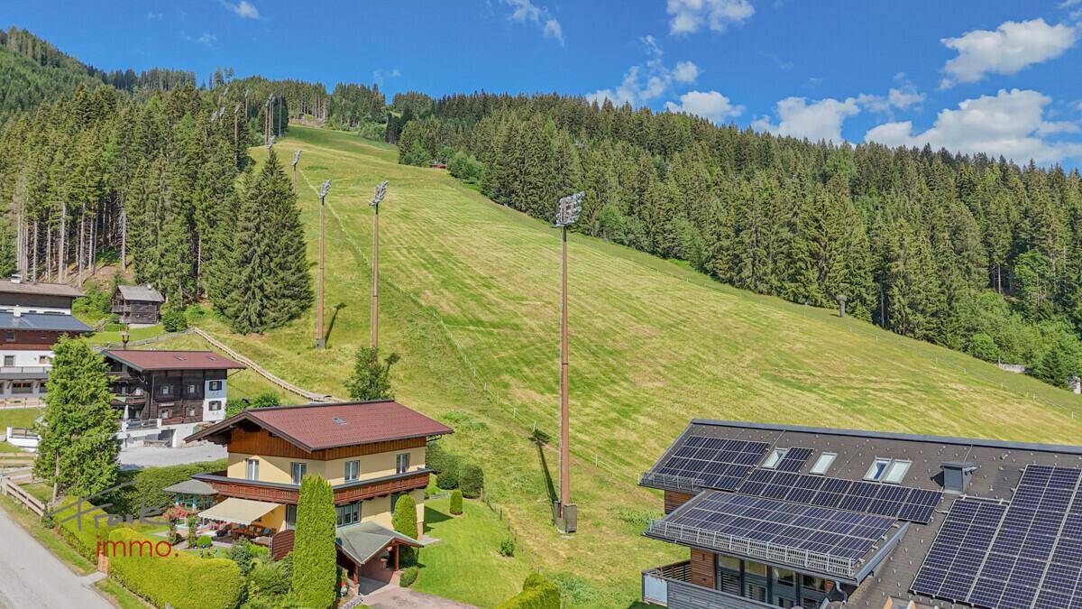 Sommerliche Luftaufnahme eines Gebäudes mit Solaranlage und Blick auf die grüne Berglandschaft.