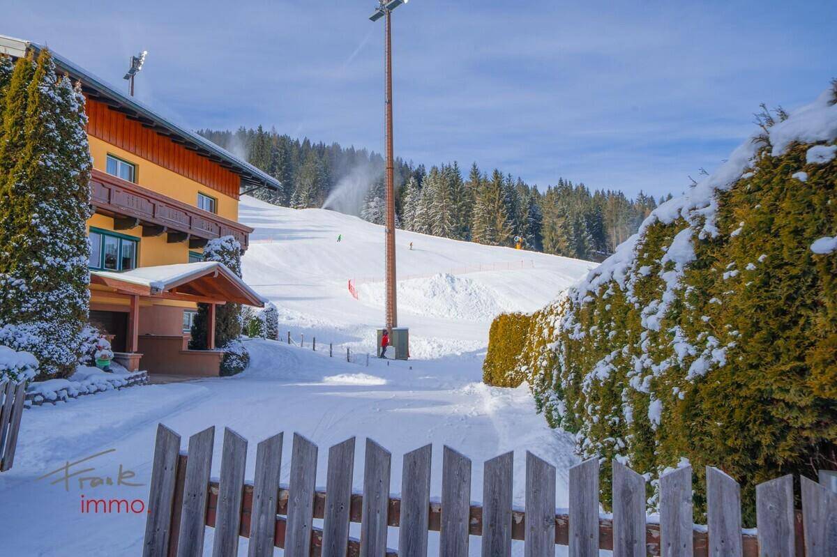 Winterliche Außenansicht eines Gebäudes mit Blick auf die verschneite Skipiste.