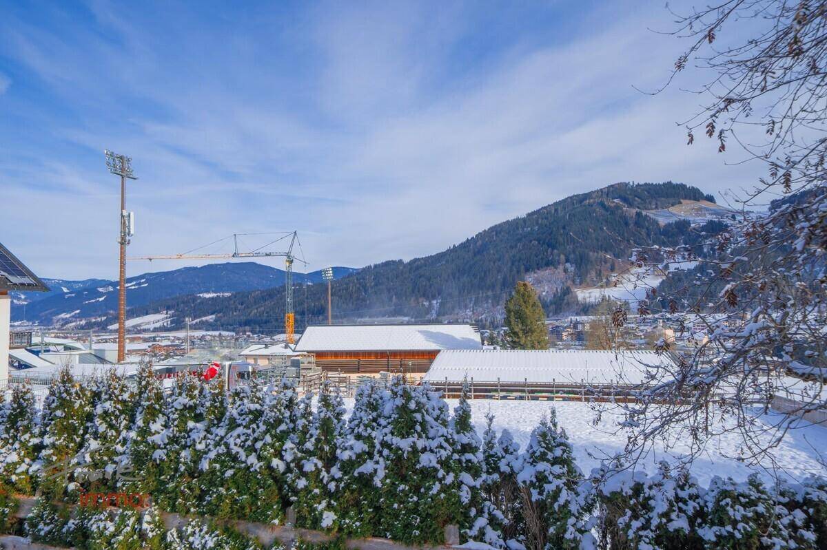 Winterlicher Ausblick auf die verschneite Ortschaft mit Bergen und einem Baukran im Hintergrund.