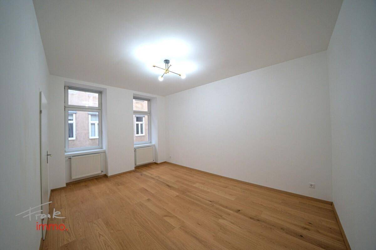 Heller, leerer Raum mit neuem Holzparkettboden und zwei Fenstern.
