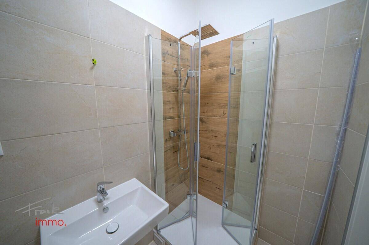 Modernes Badezimmer mit Duschkabine, Regenbrause und hellem Fliesenboden.