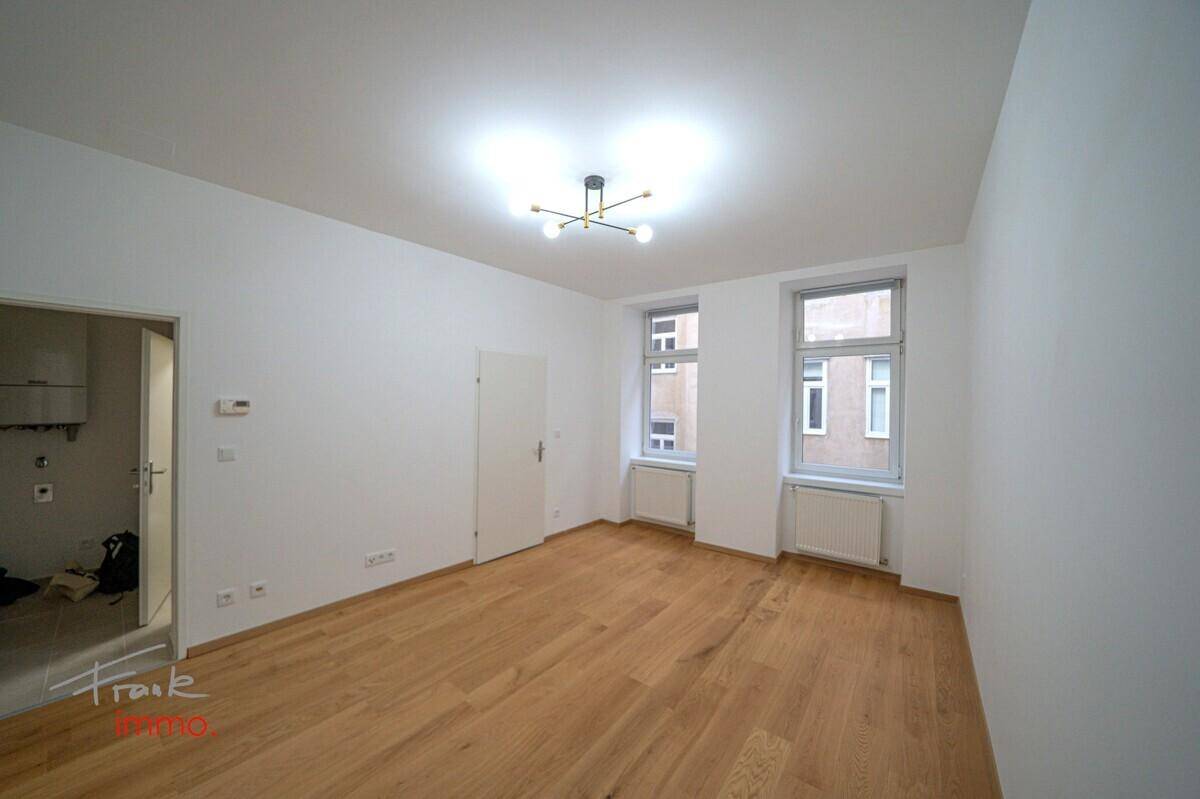 Geräumiger, heller Raum mit Holzboden und Zugang zu einem weiteren Zimmer.