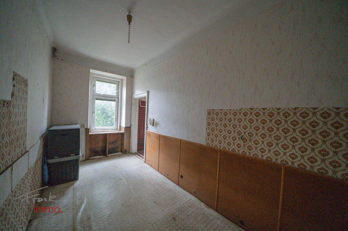Unmöblierter Raum mit alter Tapete, Fenster und sichtbaren Spuren der Abnutzung.