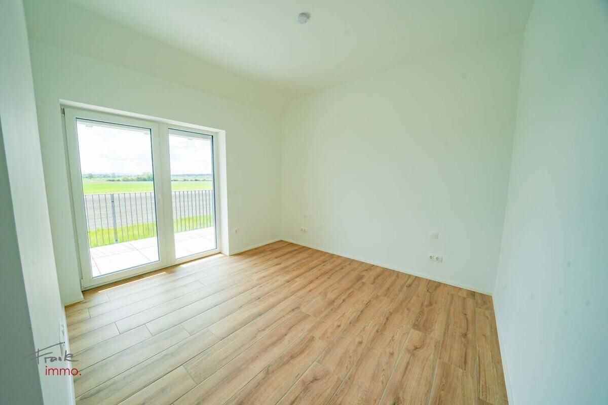 Helles Zimmer mit Holzoptik-Fliesenboden und großem Fenster mit Blick ins Grüne.