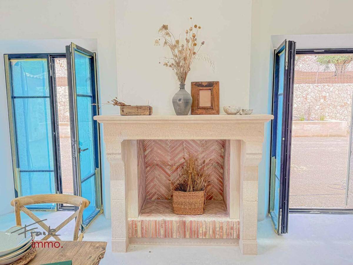 Eleganter Steinkamin mit dekorativen Elementen, umrahmt von großen Fenstern.