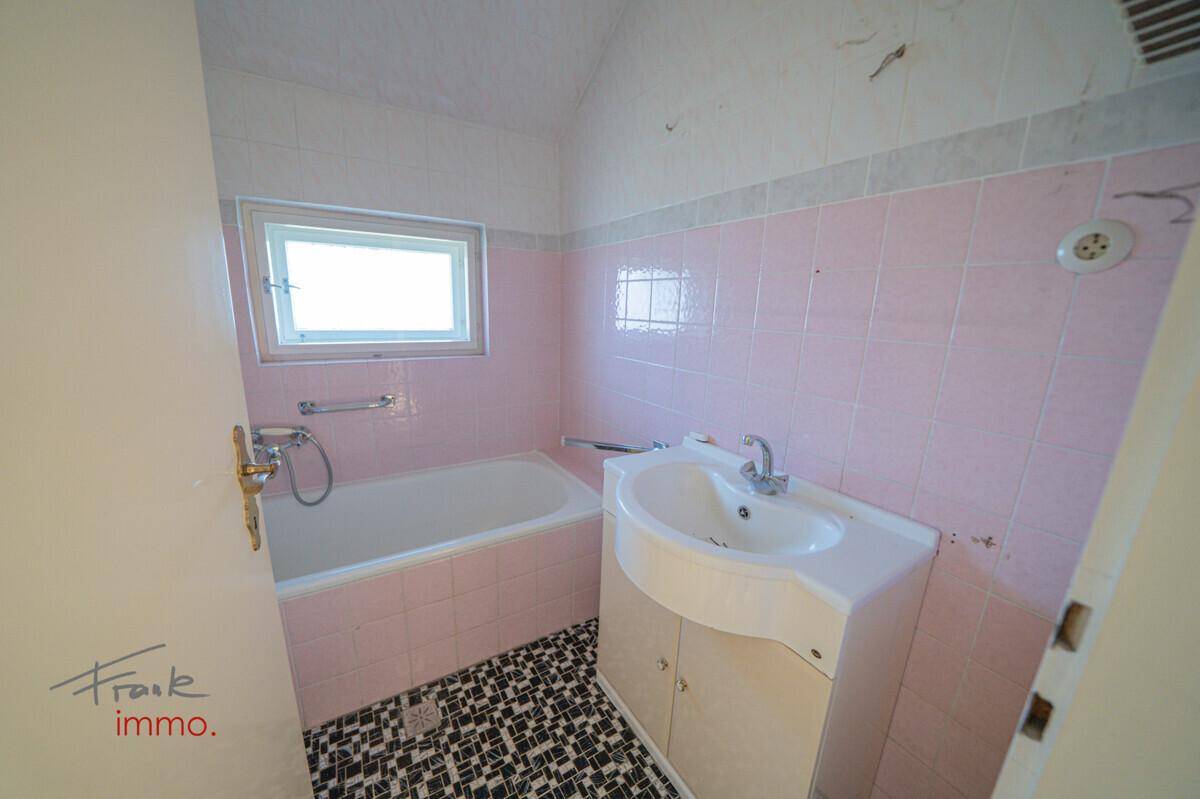 Rosa gefliestes Badezimmer mit Badewanne, Einzelwaschbecken und Fenster, bereit zur Modernisierung.