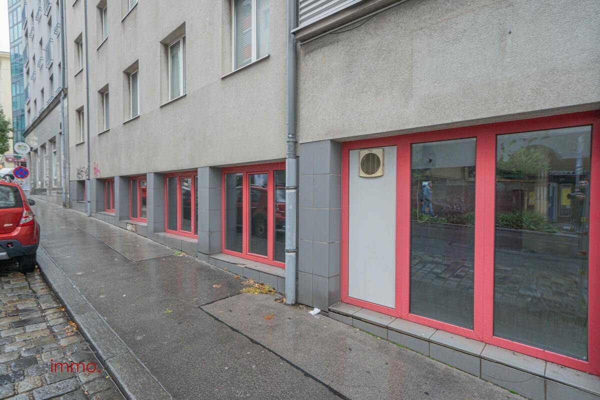 Außenansicht des Gebäudes mit roten Fensterrahmen und einem Eingangsbereich an der Straßenseite.