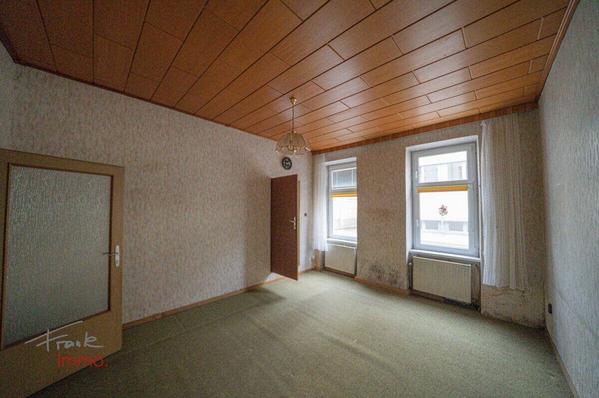 Leeres Zimmer mit Teppichboden und Holzpaneeldecke, bereit für eine Modernisierung.