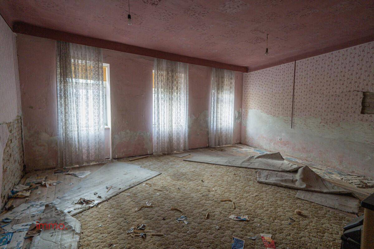 Stark renovierungsbedürftiger Raum mit Teppichboden, rosa Wänden und mehreren Fenstern.