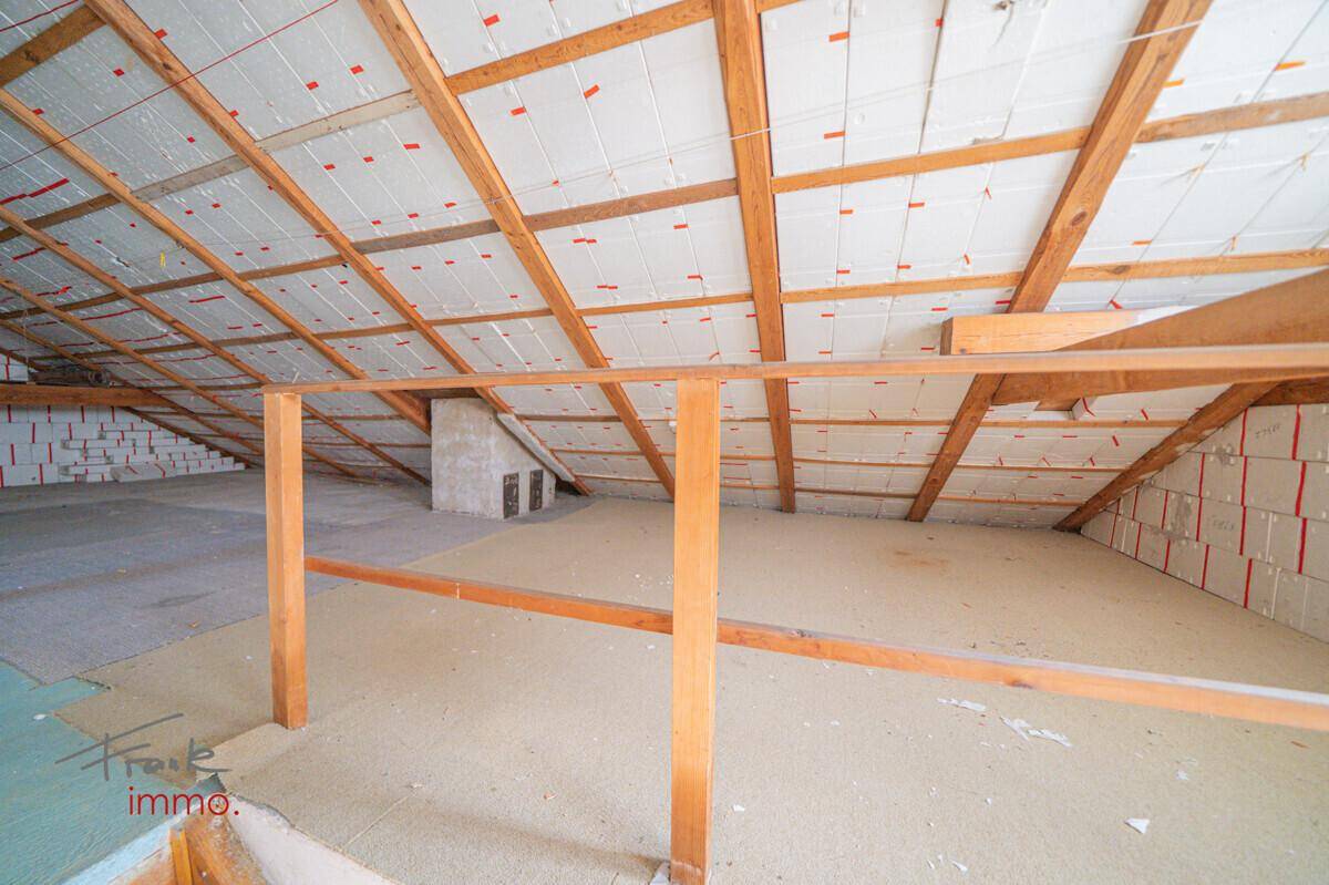 Unausgebauter Dachboden mit sichtbaren Holzbalken und Isolierung, bietet Ausbaupotenzial.