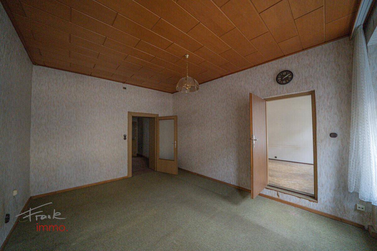 Raum mit Teppichboden, Holzpaneeldecke und einer Tür, die zu einem weiteren Zimmer führt.